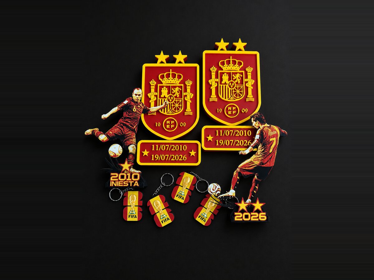 Dos escudos de la selección española impresos en 3D en relieve rojo y amarillo, con placas de fecha, siluetas de jugadores y llaveros a juego sobre fondo negro