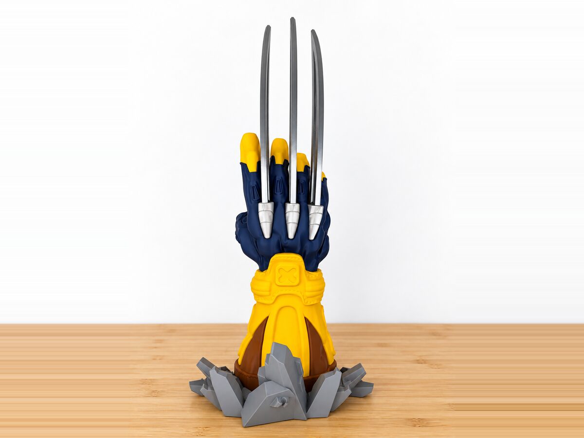 Soporte de mando con forma de garra azul y amarilla con cuchillas plateadas, impreso en 3D a varios colores sobre una peana de roca gris