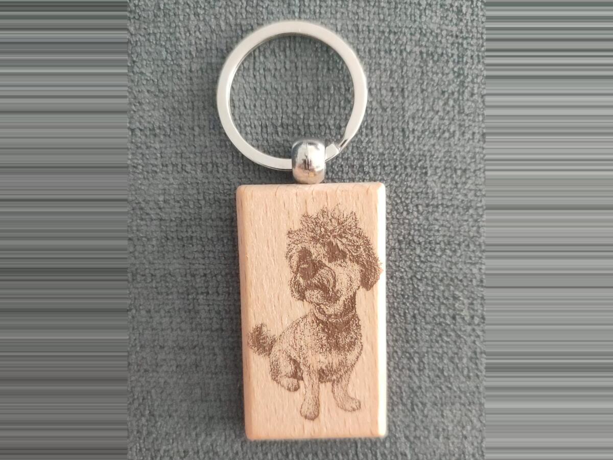 Llavero rectangular de madera clara con el retrato de un perro grabado a láser, con su anilla metálica