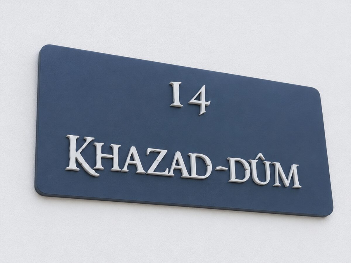 Placa azul impresa en 3D con el número y el nombre de una casa en letras blancas en relieve, montada sobre una pared blanca