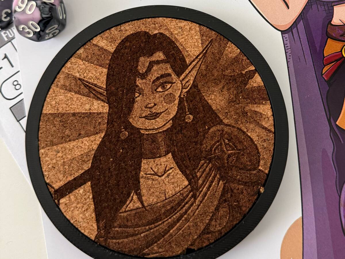 Posavasos de corcho con el retrato grabado de un personaje élfico, apoyado sobre su ficha de personaje y unos dados