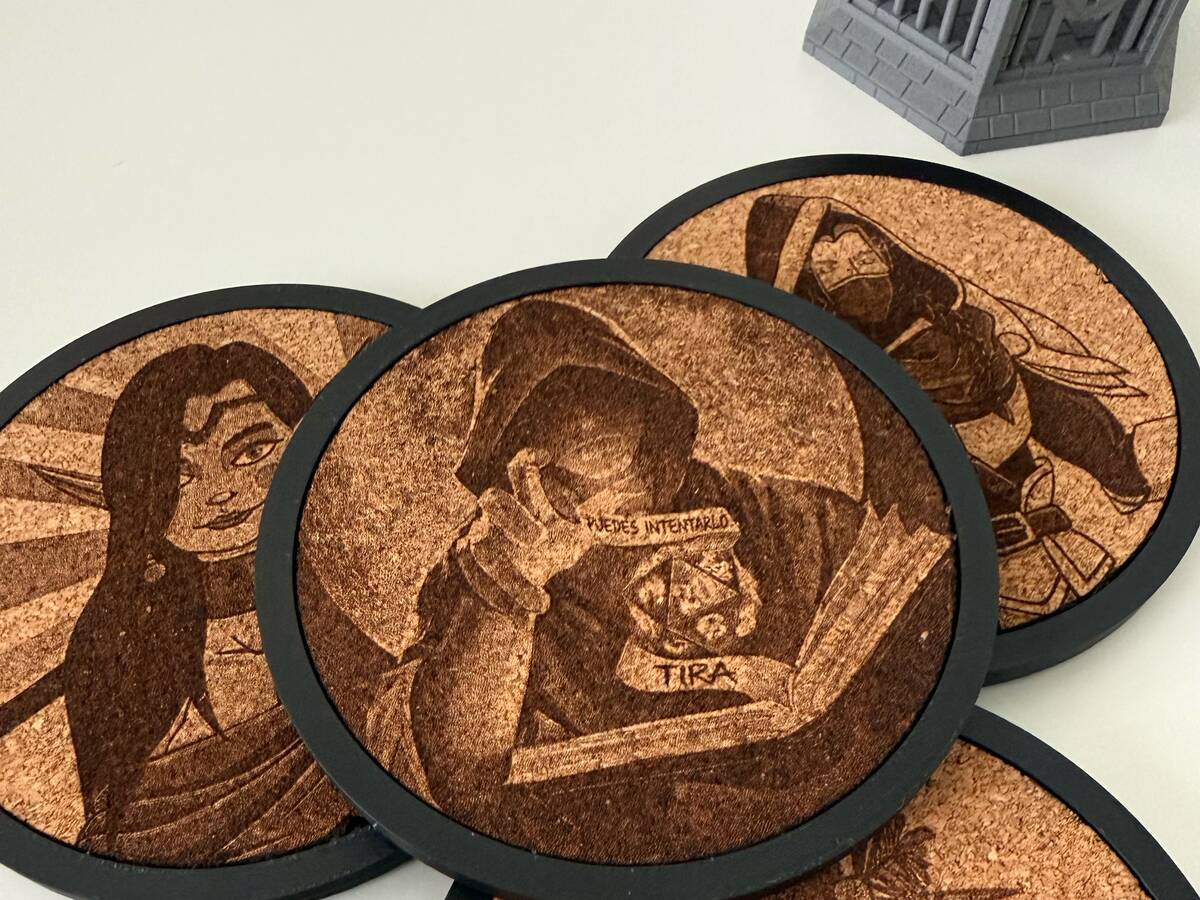 Cuatro posavasos de corcho con retratos de personajes de rol grabados a láser, cada uno con su marco impreso en 3D en negro, junto a unos dados