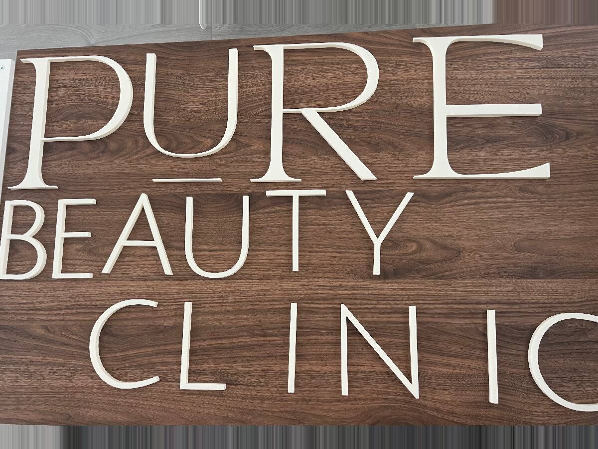 Letras del rótulo de una clínica de estética impresas en 3D en color hueso, montadas sobre un panel de madera oscura