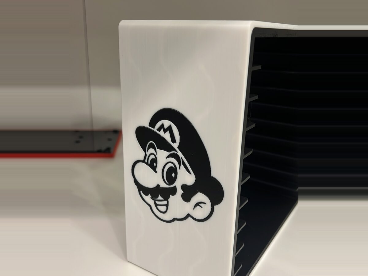 Torre organizadora de juegos impresa en 3D en blanco, con un personaje en negro a dos colores en el frontal y ranuras para los cartuchos en el lateral